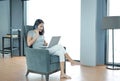 Young beautiful asian woman using mobile phone and laptop computer working online at home and feel relaxing on armchair Royalty Free Stock Photo