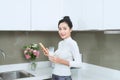 Young beautiful Asian woman using phone and drinking milk while standing in kitchen Royalty Free Stock Photo