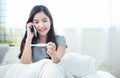 Young beautiful asian woman using smart mobile phone hand holding positive pregnancy test with smile and happy sitting on bed in Royalty Free Stock Photo