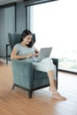 Young beautiful asian woman using smartphone and laptop computer working online at home and feel relaxing on armchair Royalty Free Stock Photo