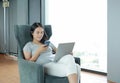 Young beautiful asian woman using smartphone and laptop computer working online at home and feel relaxing on armchair. People Royalty Free Stock Photo