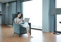 Young beautiful asian woman using smartphone and laptop computer working online at home and feel relaxing on armchair. People Royalty Free Stock Photo