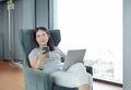 Young beautiful asian woman using smartphone and laptop computer working online at home and feel relaxing on armchair. People Royalty Free Stock Photo