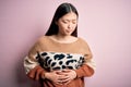 Young beautiful asian woman wearing animal print fashion sweater over pink isolated background with hand on stomach because