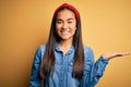 Young beautiful asian woman wearing casual denim shirt and diadem over yellow background smiling cheerful presenting and pointing Royalty Free Stock Photo