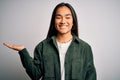 Young beautiful asian woman wearing casual shirt standing over isolated white background smiling cheerful presenting and pointing Royalty Free Stock Photo