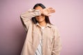 Young beautiful asian woman wearing casual shirt standing over pink background covering eyes with arm, looking serious and sad Royalty Free Stock Photo