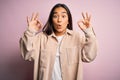 Young beautiful asian woman wearing casual shirt standing over pink background looking surprised and shocked doing ok approval Royalty Free Stock Photo