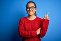 Young beautiful asian woman wearing casual sweater and glasses over blue background with a big smile on face, pointing with hand Royalty Free Stock Photo