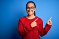 Young beautiful asian woman wearing casual sweater and glasses over blue background smiling and looking at the camera pointing Royalty Free Stock Photo