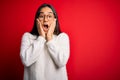 Young beautiful asian woman wearing casual sweater and glasses over red background afraid and shocked, surprise and amazed Royalty Free Stock Photo