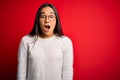 Young beautiful asian woman wearing casual sweater and glasses over red background afraid and shocked with surprise and amazed Royalty Free Stock Photo