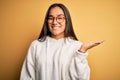 Young beautiful asian woman wearing casual sweater and glasses over yellow background smiling cheerful presenting and pointing Royalty Free Stock Photo