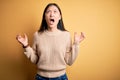 Young beautiful asian woman wearing casual sweater over yellow isolated background crazy and mad shouting and yelling with