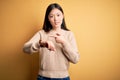 Young beautiful asian woman wearing casual sweater over yellow isolated background In hurry pointing to watch time, impatience,