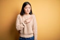 Young beautiful asian woman wearing casual sweater over yellow isolated background Pointing aside worried and nervous with