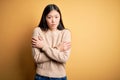 Young beautiful asian woman wearing casual sweater over yellow isolated background shaking and freezing for winter cold with sad