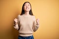 Young beautiful asian woman wearing casual sweater over yellow isolated background very happy and excited doing winner gesture Royalty Free Stock Photo