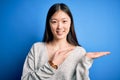 Young beautiful asian woman wearing casual sweater standing over blue isolated background amazed and smiling to the camera while Royalty Free Stock Photo