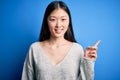 Young beautiful asian woman wearing casual sweater standing over blue isolated background with a big smile on face, pointing with Royalty Free Stock Photo