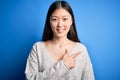 Young beautiful asian woman wearing casual sweater standing over blue isolated background cheerful with a smile on face pointing Royalty Free Stock Photo