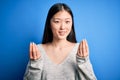 Young beautiful asian woman wearing casual sweater standing over blue isolated background doing money gesture with hands, asking Royalty Free Stock Photo