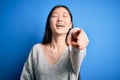 Young beautiful asian woman wearing casual sweater standing over blue isolated background laughing at you, pointing finger to the Royalty Free Stock Photo