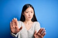 Young beautiful asian woman wearing casual sweater standing over blue isolated background Moving away hands palms showing refusal