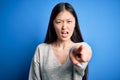 Young beautiful asian woman wearing casual sweater standing over blue isolated background pointing displeased and frustrated to Royalty Free Stock Photo