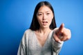 Young beautiful asian woman wearing casual sweater standing over blue isolated background pointing displeased and frustrated to Royalty Free Stock Photo