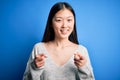 Young beautiful asian woman wearing casual sweater standing over blue isolated background pointing fingers to camera with happy Royalty Free Stock Photo