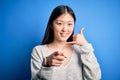 Young beautiful asian woman wearing casual sweater standing over blue isolated background smiling doing talking on the telephone Royalty Free Stock Photo