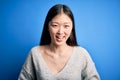 Young beautiful asian woman wearing casual sweater standing over blue isolated background smiling and laughing hard out loud Royalty Free Stock Photo