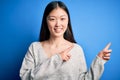 Young beautiful asian woman wearing casual sweater standing over blue isolated background smiling and looking at the camera Royalty Free Stock Photo