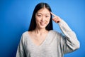 Young beautiful asian woman wearing casual sweater standing over blue isolated background Smiling pointing to head with one Royalty Free Stock Photo