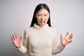 Young beautiful asian woman wearing casual sweater standing over isolated background crazy and mad shouting and yelling with
