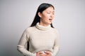 Young beautiful asian woman wearing casual sweater standing over isolated background with hand on stomach because nausea, painful