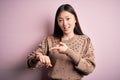 Young beautiful asian woman wearing fashion and elegant sweater over pink solated background In hurry pointing to watch time,