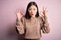 Young beautiful asian woman wearing fashion and elegant sweater over pink solated background looking surprised and shocked doing Royalty Free Stock Photo