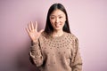 Young beautiful asian woman wearing fashion and elegant sweater over pink solated background showing and pointing up with fingers