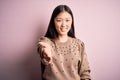 Young beautiful asian woman wearing fashion and elegant sweater over pink solated background smiling cheerful offering palm hand