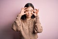 Young beautiful asian woman wearing fashion and elegant sweater over pink solated background Trying to open eyes with fingers,