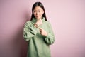 Young beautiful asian woman wearing green winter sweater over pink solated background In hurry pointing to watch time, impatience,