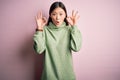 Young beautiful asian woman wearing green winter sweater over pink solated background looking surprised and shocked doing ok Royalty Free Stock Photo