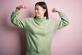 Young beautiful asian woman wearing green winter sweater over pink solated background showing arms muscles smiling proud