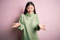 Young beautiful asian woman wearing green winter sweater over pink solated background smiling cheerful with open arms as friendly