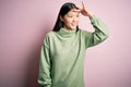 Young beautiful asian woman wearing green winter sweater over pink solated background very happy and smiling looking far away with Royalty Free Stock Photo