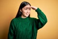 Young beautiful asian woman wearing green winter sweater over yellow  background very happy and smiling looking far away Royalty Free Stock Photo