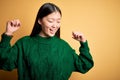 Young beautiful asian woman wearing green winter sweater over yellow isolated background Dancing happy and cheerful, smiling Royalty Free Stock Photo