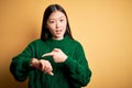 Young beautiful asian woman wearing green winter sweater over yellow isolated background In hurry pointing to watch time,